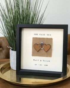 a couple's wedding rings are displayed in a shadow box on a table next to a potted plant