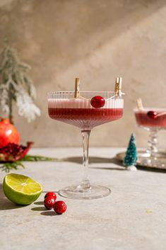 two glasses filled with drinks sitting on top of a table next to limes and cranberries