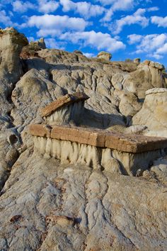 an old bench sitting on top of a rocky hill under a blue sky with clouds