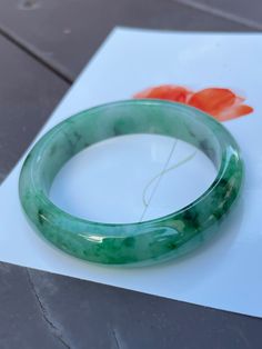 Deeper green hues are mixed with vibrant green hues in this Type A jade bangle. The mix of green hues is spread across the body of the green jade bangle giving it a refined appearance. In jadeite, such flowing patterns with its alluring blend of colours is like an art design, albeit created by nature. In the areas without the more vivid hues of green, the jade bangle has a light green base colour. A fine crystal aggregate structure is present in the entire jadeite bangle. The deeply polished fin Affordable Handmade Green Bangle, Luxury Jade Bangle Bracelet, Luxury Jade Bangle Jewelry, Luxury Handmade Green Bangle, Cheap Handmade Green Bangle, Cheap Green Round Bangle, Affordable Jade Bangle Jewelry, Cheap Green Bangle Jewelry, Cheap Green Bangle For Women