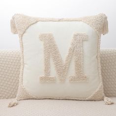 a white pillow with the letter m on it and tassels around the edges