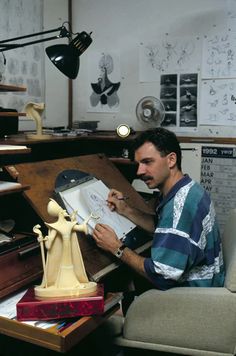 a man sitting at a desk working on a piece of paper with a lamp in the background