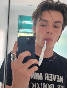 a young man taking a selfie in front of a mirror while brushing his teeth