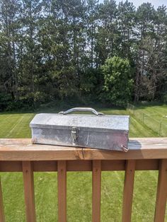 an old metal box sitting on top of a wooden rail next to a green field