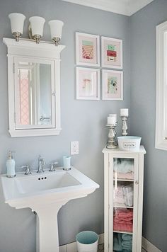 a white pedestal sink sitting under a bathroom mirror next to a cabinet filled with towels