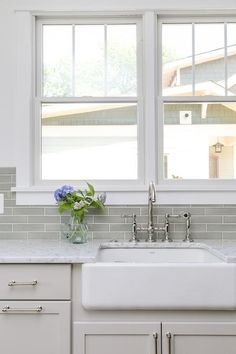 a white kitchen sink sitting under two windows next to a window sill with flowers in it