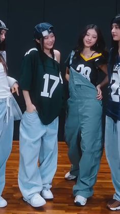 three girls in overalls are standing on a stage with one girl wearing a football jersey