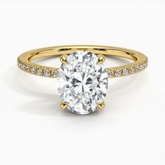 a yellow gold engagement ring with an oval cut diamond in the center and pave set shoulders