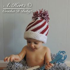 a baby in a crochet hat sitting on a blanket holding a pair of scissors