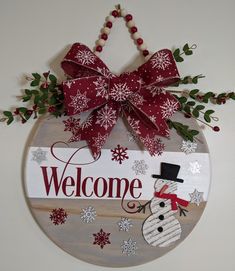 a welcome sign with a snowman and red bow hanging from the side of a wall