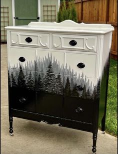 an old dresser has been painted with black and white trees on the front, and is sitting outside