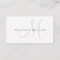 a white business card with the letter m in grey ink on it, sitting on top of a marble surface