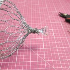 wire wrapped around the ends of scissors on a pink table with grids and other crafting supplies