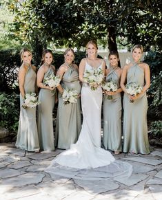 a group of women standing next to each other in front of some bushes and trees