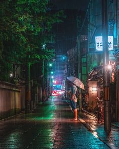 a person with an umbrella is standing in the rain on a city street at night