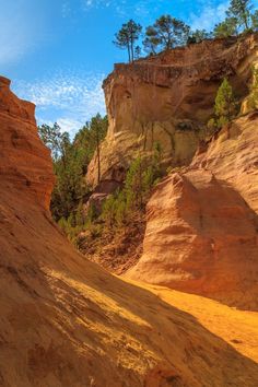 the sun shines on some red rocks and trees in the distance, with blue skies above