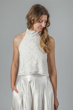 "The 'Aster' halter neck top This halter neck top is handmade in off-white cotton lace, lined in a soft organic cotton jersey. The neck tie is in organic cotton/ silk satin, which has a gentle sheen to it. The ties can be be tied at the back of the neck with a bow or left long. The top closes at the back with little covered buttons and rouleaux loops. This top is individually made to order in sizes XXS - XXL, please refer to size chart below. It can also be made to custom sizes/lengths. For sizing advice or to submit your measurements please get in touch.  It is available to order in off-white/ ivory. The standard length is 18\" from shoulder to hem. Made from 95% cotton, 5% nylon. Lined in 100% organic cotton jersey.  This top is made to order, designed, cut and stitched by me in England. Elegant Cropped Top With Delicate Lace, Elegant High Neck Lace Top, Elegant Scalloped Lace Cropped Top, White Delicate Lace Cropped Top, Elegant Cropped Lace Top With Scalloped Edges, Delicate Lace Cropped Top For Party, Fitted Lace Halter Neck Top, Fitted Halter Neck Top For Wedding, Fitted Halter Neck Lace Top