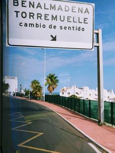 a street sign on the side of a road with palm trees and buildings in the background