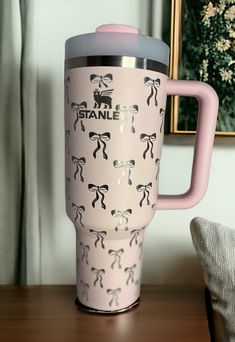 a pink travel mug sitting on top of a wooden table next to a framed painting