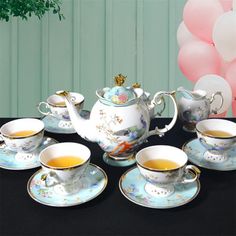 there is a tea set with cups and saucers on the table next to balloons