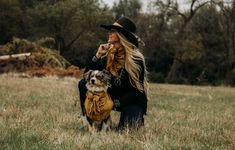 a woman sitting in the grass with her dog wearing a bandana and holding it