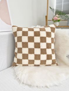 a brown and white checkered pillow sitting on top of a bed next to a plant