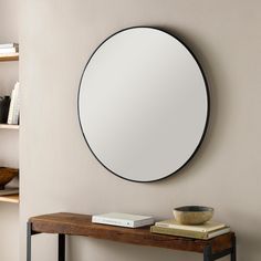 a round mirror hanging on the wall above a wooden table with a bowl and books