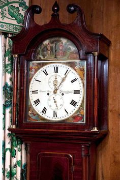 an old grandfather clock with roman numerals on the face and hands, in front of curtains