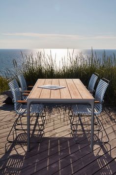 a wooden table sitting on top of a wooden deck next to tall grass and water