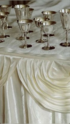 silver goblets are lined up on a white table cloth for a wedding reception