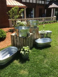 several metal buckets and planters on the grass in front of a brick building