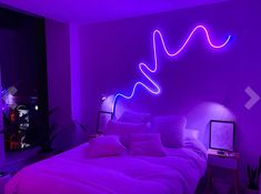 a bed in a room with purple lights on the wall and white linens under it