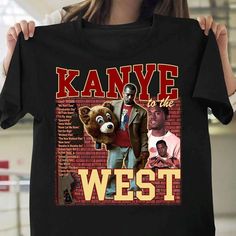 a woman holding up a black t - shirt with the words kanye to me west on it