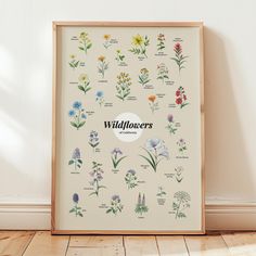 a framed poster with wildflowers on it in front of a white wall and wooden floor