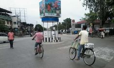 two people riding bikes down the street in front of a billboard on a pole with an advertisement