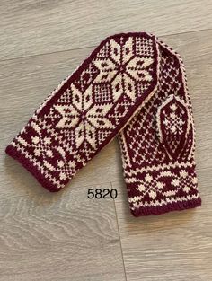 two red and white knitted mittens sitting on top of a wooden floor next to each other