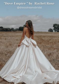 a woman in a wedding dress standing in a field with her back to the camera