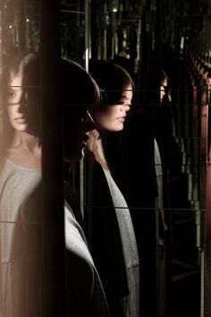 two women standing in front of a mirror looking at their own reflection on the wall