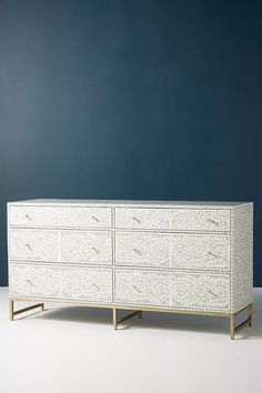 a white dresser with gold handles against a blue wall