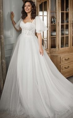 a woman in a white wedding dress standing next to a wooden china cabinet and wearing a tiara