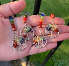 a person holding three different colored beads in their hand with tree of life charms on them