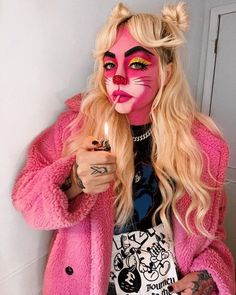 a woman with pink makeup holding a lit candle in her hand and wearing a cat costume