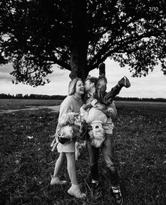 black and white photograph of three children standing under a tree with stuffed animals on their shoulders