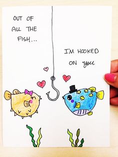 someone holding up a card with two fish and a fishing hook attached to it, which says out of all the fish i'm hooked on you