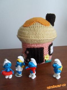 crocheted smurf with small figures around it on a wooden table next to a cupcake