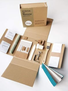 an open cardboard box with scissors, tape and other items in it on a white surface