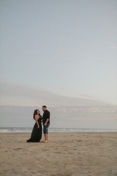 a man and woman standing on top of a sandy beach