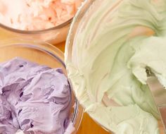 two bowls filled with purple and green frosting on top of a wooden table next to each other