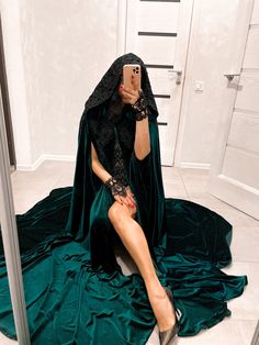 a woman sitting on the floor taking a selfie with her cell phone wearing a green cloak