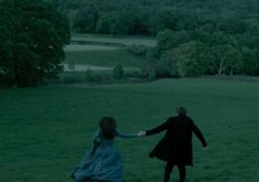 two people holding hands in a field with trees and hills in the background at night